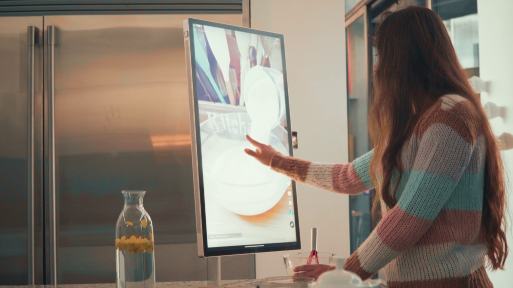Mujer usando pantalla táctil inteligente Wandr para seguir receta en cocina moderna.